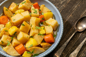 Turkish-style braised celeriac (Zeytinyağlı kereviz) in bowl on rustic wooden table. Knife and fork next to it. 