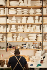 Ceramist working at a bench under shelves full of pottery molds