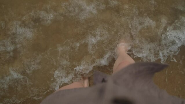Barefoot female legs washed by waves on ocean shore.