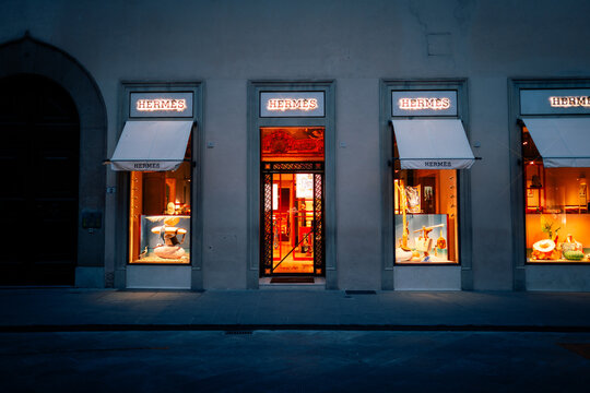 Florence, Italy - August 29 2023 : Front entrance of the luxury fashion brand store Hermes, famous for their handbags, with signage, logo and canopy, shop windows. Horizontal landscape format at night