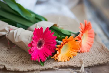 Fototapeten bright gerbera flowers wrapped in paper sitting on a rustic mat © Alfazet Chronicles
