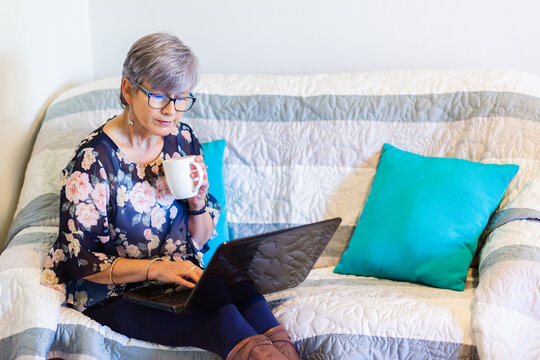 senior woman working on laptop on lounge with a cup of tea