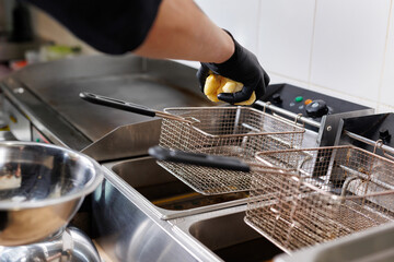 The cook is cooking French fries. Frying potatoes in fryer for french fries.