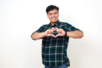 Excited young asian man standing while showing love heart shape with his hands