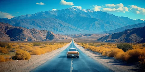 Poster Oldtimer vintage car driving along a straight road in the arid desert toward a beautiful montain landscape © acrogame
