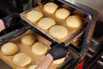 The chef puts a baking tray with burger buns baked in the oven.