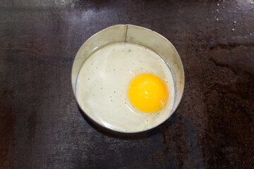 Fried egg in stainless steel mood ring on hot pan.