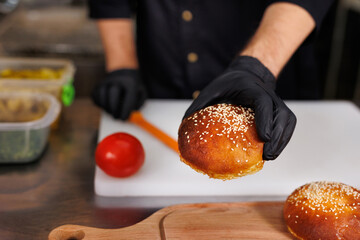 Cook in the kitchen is slicing burger buns.