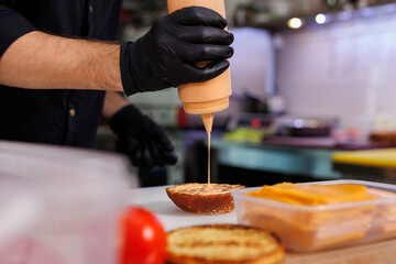 Cooking a burger on the grill. Spreading sauce on a burger bun.