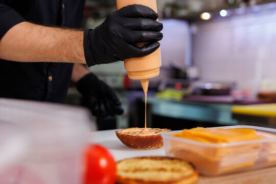 Cooking a burger on the grill. Spreading sauce on a burger bun.
