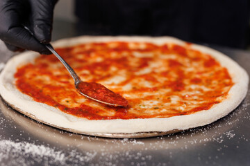 The chef spreads tomato sauce on a pizza pan.