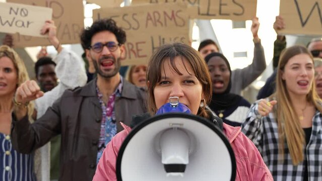 Group of multiracial peace activists walking on the street holding posters and banners - Diverse crowd of antiwar people protesting against war