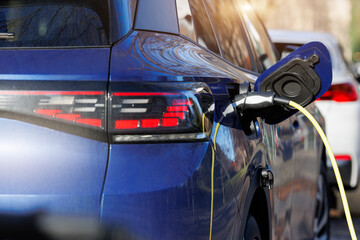 Close-up modern electric plug-in hybrid car parked near fast charger charging station point in...