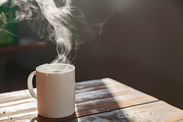 Steam from hot mug of tea on picnic bench in the morning light