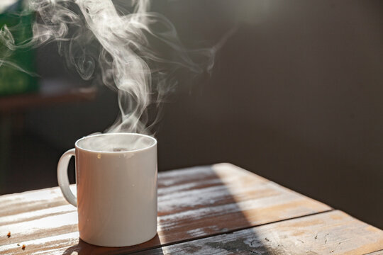 Steam from hot mug of tea on picnic bench in the morning light
