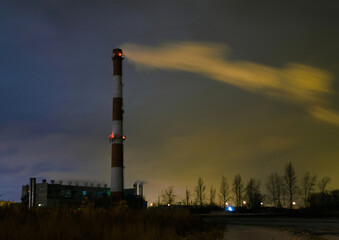 View of the boiler room with a high chimney and smoke from it in the middle of the night