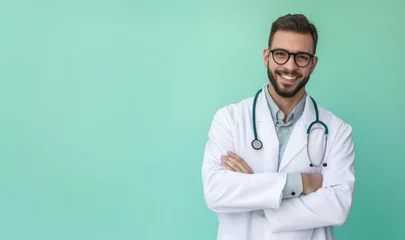 Fotobehang A smiling male doctor in a white coat with a stethoscope stands confidently with his arms crossed against a turquoise background, exuding professionalism and friendliness. © zakiroff