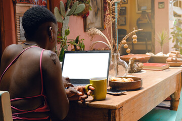 young afro woman at home sitting with laptop working and eating croissants with coffee.