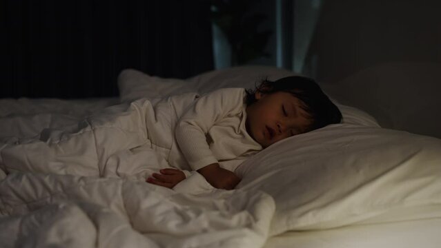 panning shot of toddler baby sleeping on a bed at night