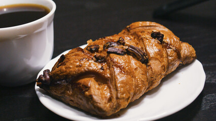 Maple pecan bun on a saucer and a cup of black coffee. Close up.