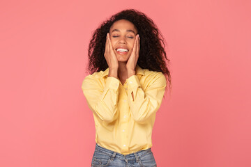Joyful black woman with hands on cheeks on pink background