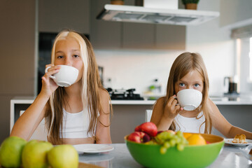 Sisters children have breakfast with tea and fruit in the kitchen