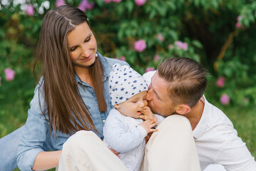 Obraz premium Happy Caucasian family with a young son relax in the park in spring or summer, sitting on a blanket. Dad kisses the boy on the cheek