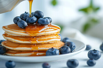 A pile of delicious blueberry pancakes with pouring maple syrup on white background. Brunch and breakfast concept.