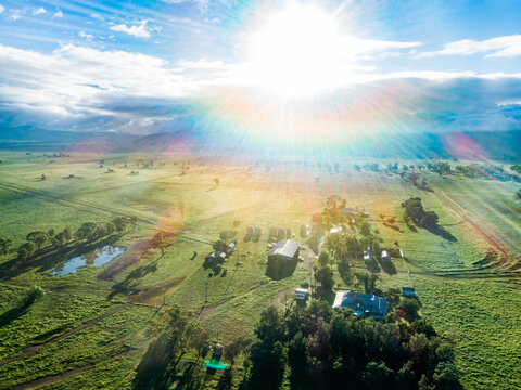 Morning sunlight bursting over small country farmstead and green paddocks