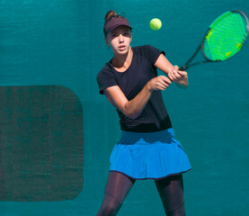 A girl plays tennis on a court with a hard blue surface on a summer sunny da