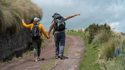 Young Latin American couple with backpacks walking holding hands on a trail in the middle of the...