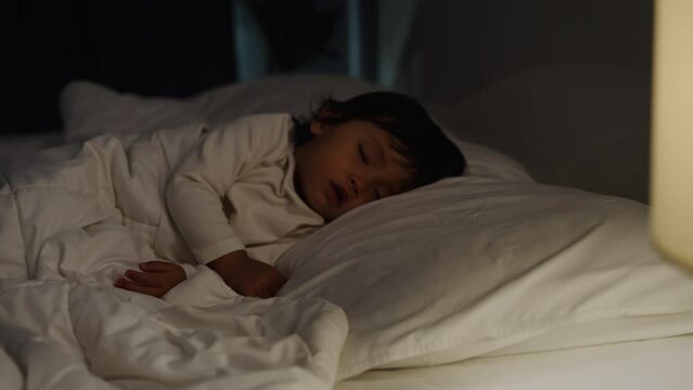 panning shot of toddler baby sleeping on a bed at night