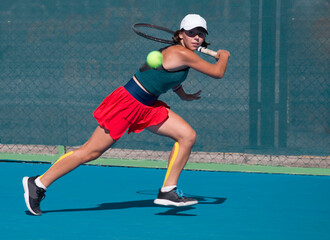 A girl plays tennis on a court with a hard blue surface on a summer sunny day	
