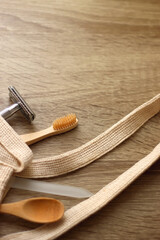 Crochet bag, wooden hairbursh, face roller, reusable razor, glass nail file, wooden toothbrush and wooden spoon on wooden background. Various zero waste products. Selective focus.