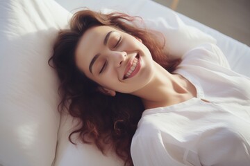 Caucasian woman reclines luxuriously on a plush, white bed and pillow. Behold the tranquil joy in her smile as her eyes emanate serenity.