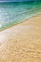Sea wave reaching the sand of the paradisiacal beach during a beautiful day of sun and turquoise water.