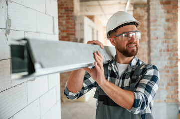 Holding metal plank. Construction worker in uniform in empty unfinished room