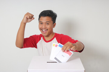 Portrait of excited Asian man inserting and putting the voting paper into the ballot box. General...