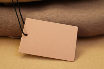 Garment with cardboard tag on kraft paper sheet, closeup. Space for text