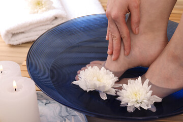 Obraz na płótnie Canvas Woman soaking her feet in bowl with water and flowers on floor, closeup. Spa treatment