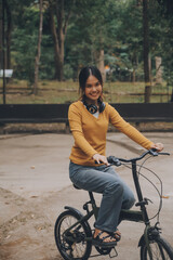 Fototapeta na wymiar Happy young Asian woman while riding a bicycle in a city park. She smiled using the bicycle of transportation. Environmentally friendly concept.