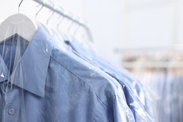 Dry-cleaning service. Many different clothes in plastic bags hanging on rack indoors, closeup