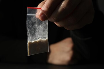 Drug addiction. Man with plastic bag of cocaine on dark background, closeup