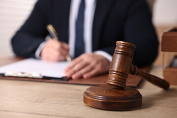 Notary writing notes at wooden table in office, focus on gavel