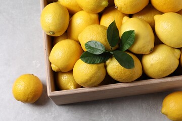 Fresh lemons in wooden crate on grey table, above view
