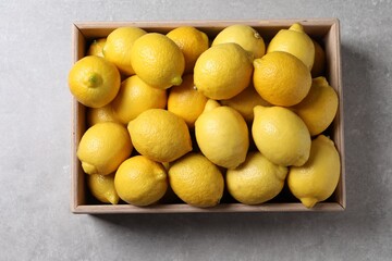 Fresh lemons in wooden crate on grey table, top view