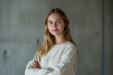 Fototapeta premium One brunette woman posing: Confident young woman in a white sweater, arms crossed, against a textured grey background.