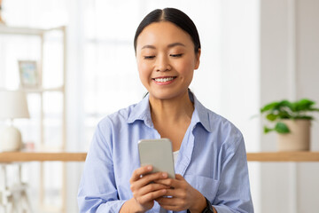 Portrait of happy chinese lady using cell phone at home