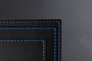 Black leather wallet with blue stitching on a black background.