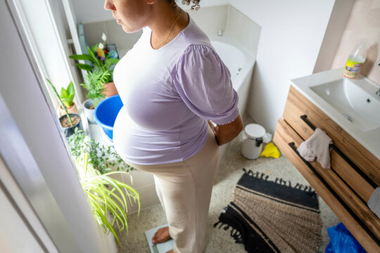 African american pregnant woman weighing herself in the bathroom